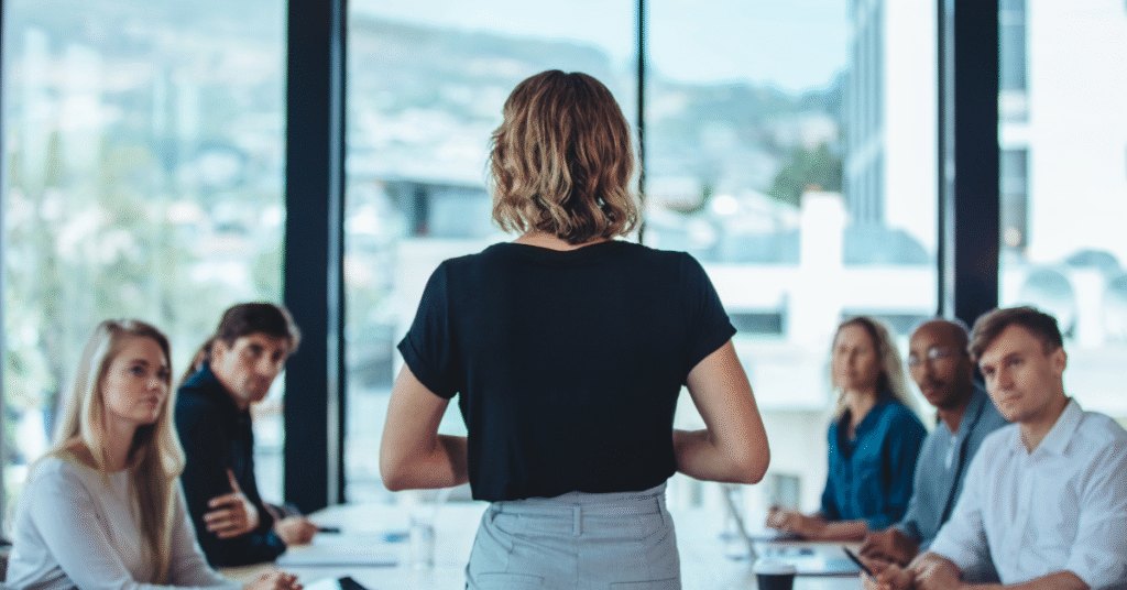 A business leader standing and speaking to a group of executives during a meeting about cybersecurity awareness.