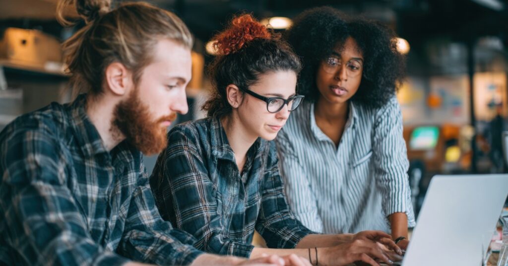 A group of three focused professionals reviewing information together on a laptop in a modern office, representing teamwork and clarity in the IT support process.